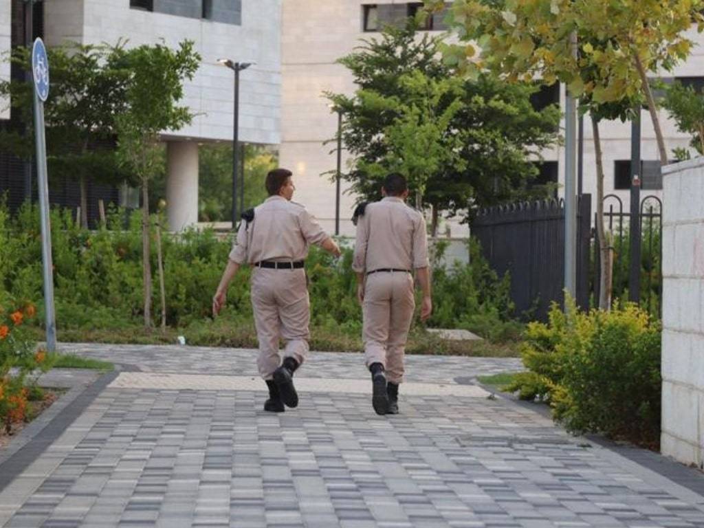 שני אנשים במדים הולכים בדרך מרוצפת ליד בניין משרדים וגינה ירוקה.