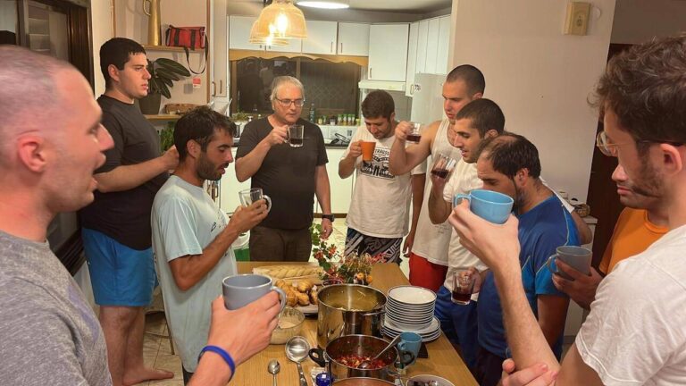 קבוצה של אנשים במטבח שותים ומדברים סביב שולחן מלא בכלים ואוכל.